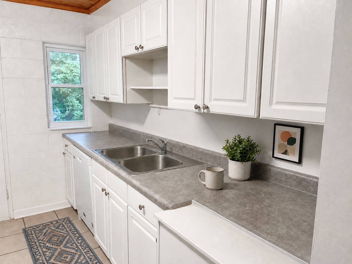 Galley kitchen with white cabinetry, stainless double sink, and window over the counter