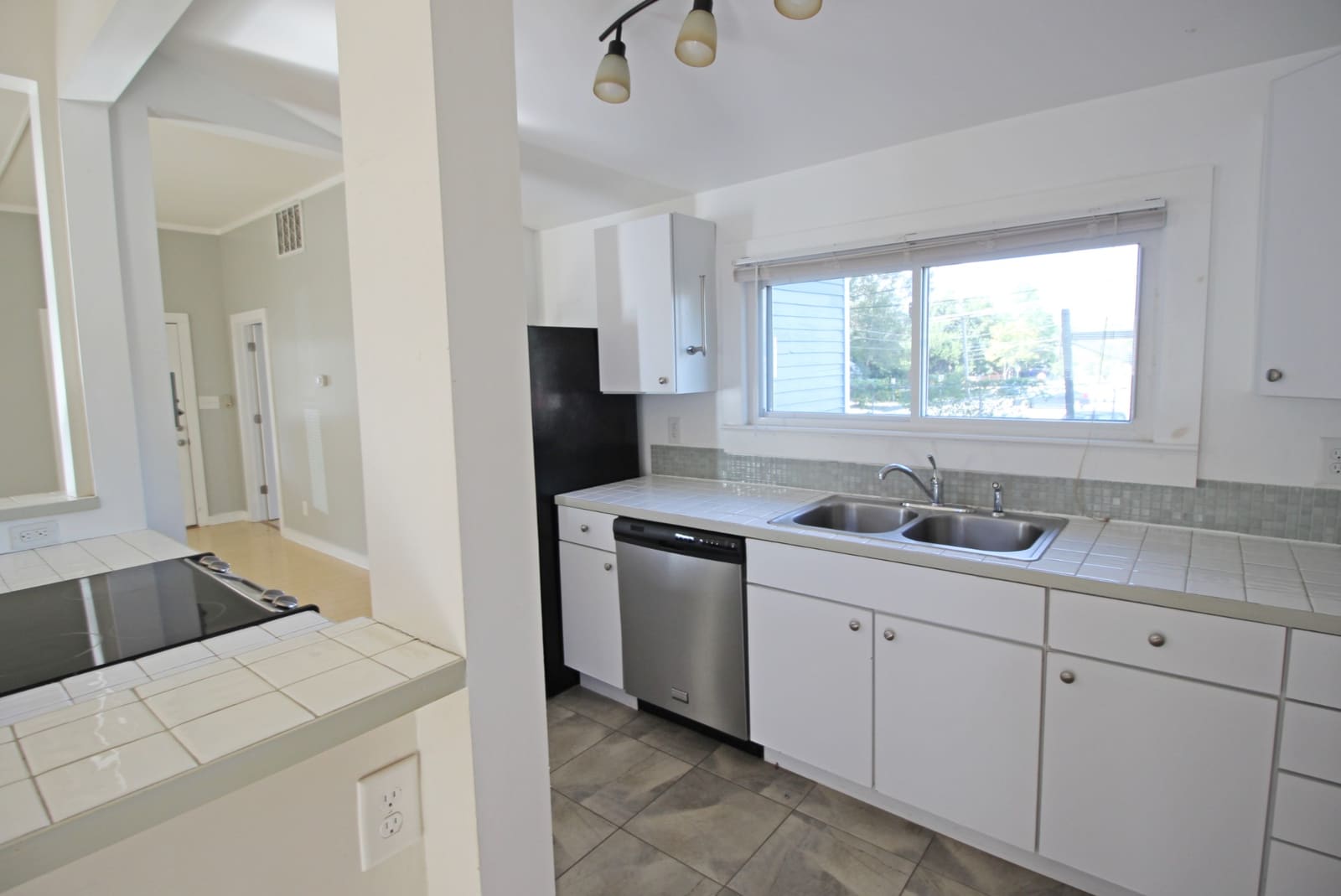 Kitchen sink under a wide window with glass-tile backsplash
