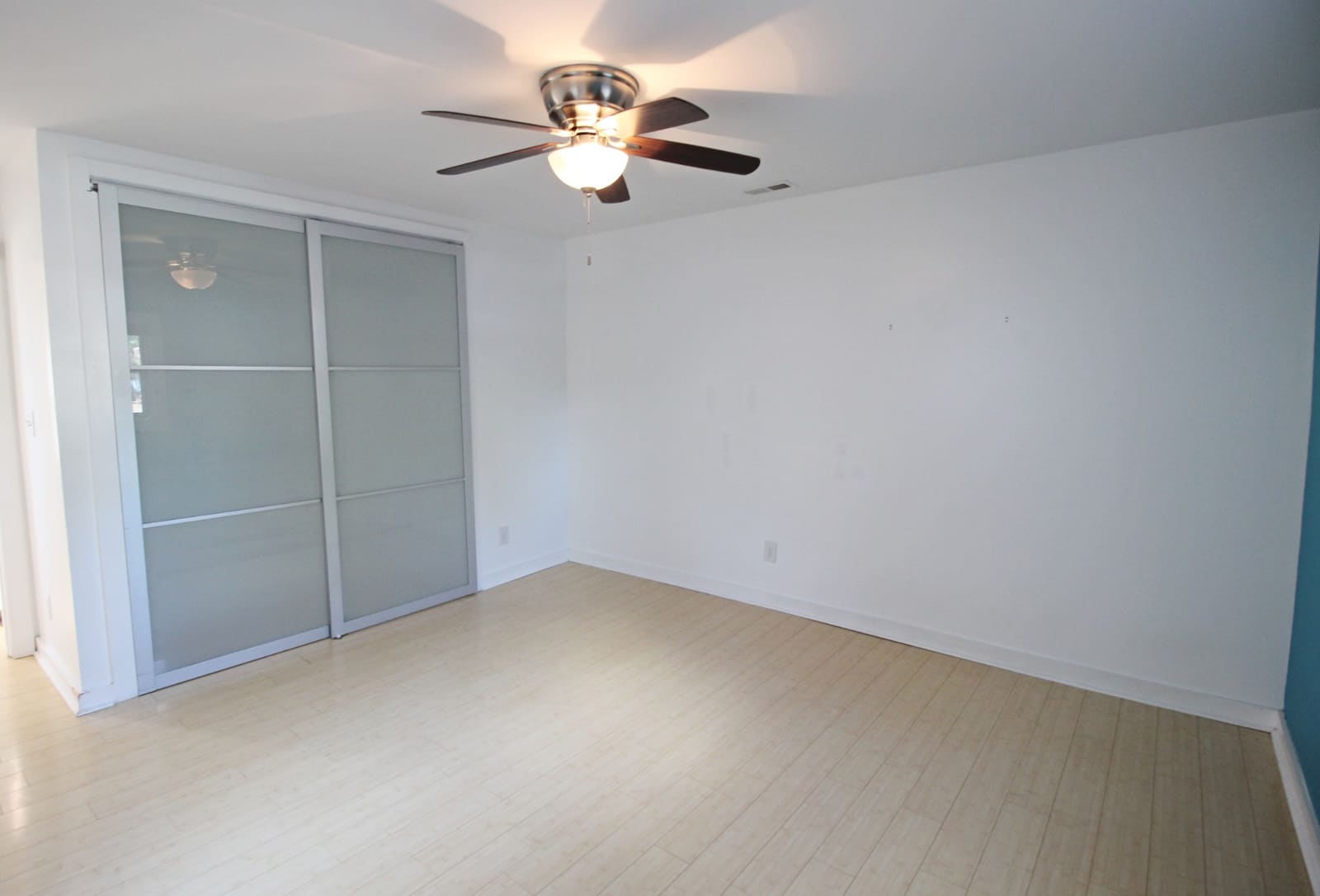 Bedroom with frosted-glass sliding closet doors, ceiling fan, and bamboo floors