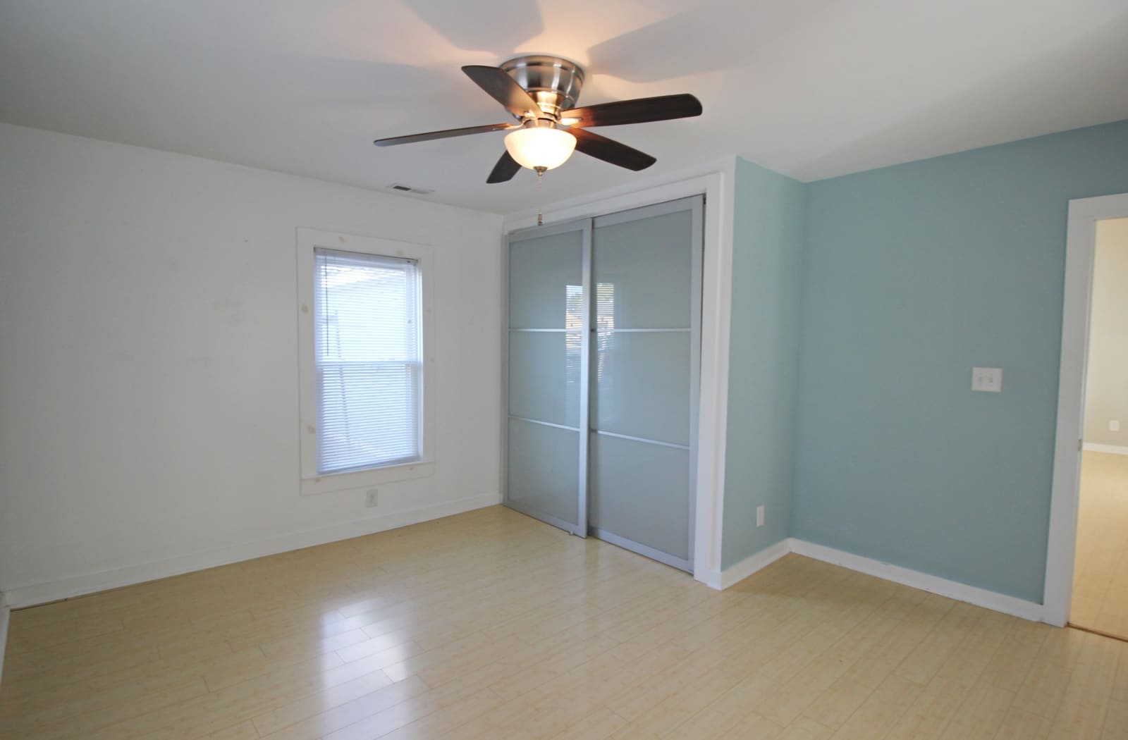 Bedroom with light blue walls, frosted sliding closet doors, and a bright window