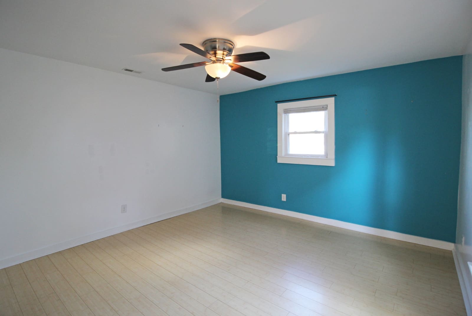 Bedroom with teal accent wall, ceiling fan, and bamboo floors