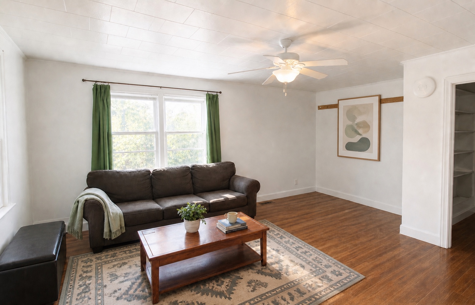 Sunlit living room with hardwood floors, ceiling fan, and double windows