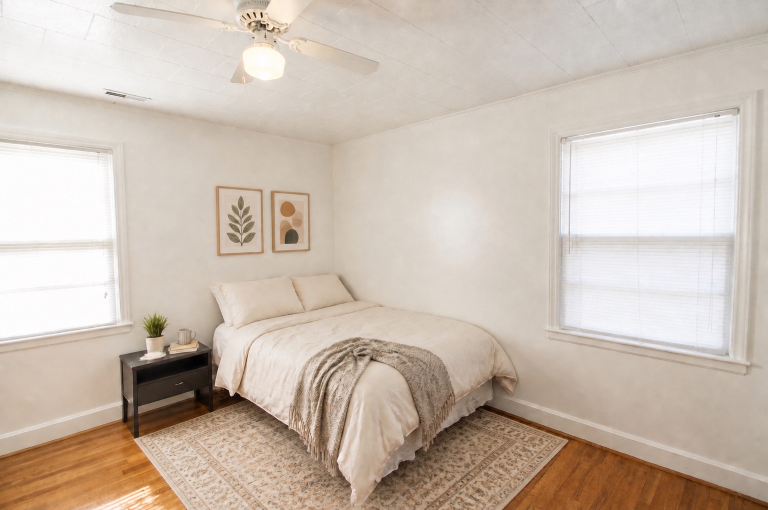 Bright bedroom with hardwood floors, ceiling fan, and two windows